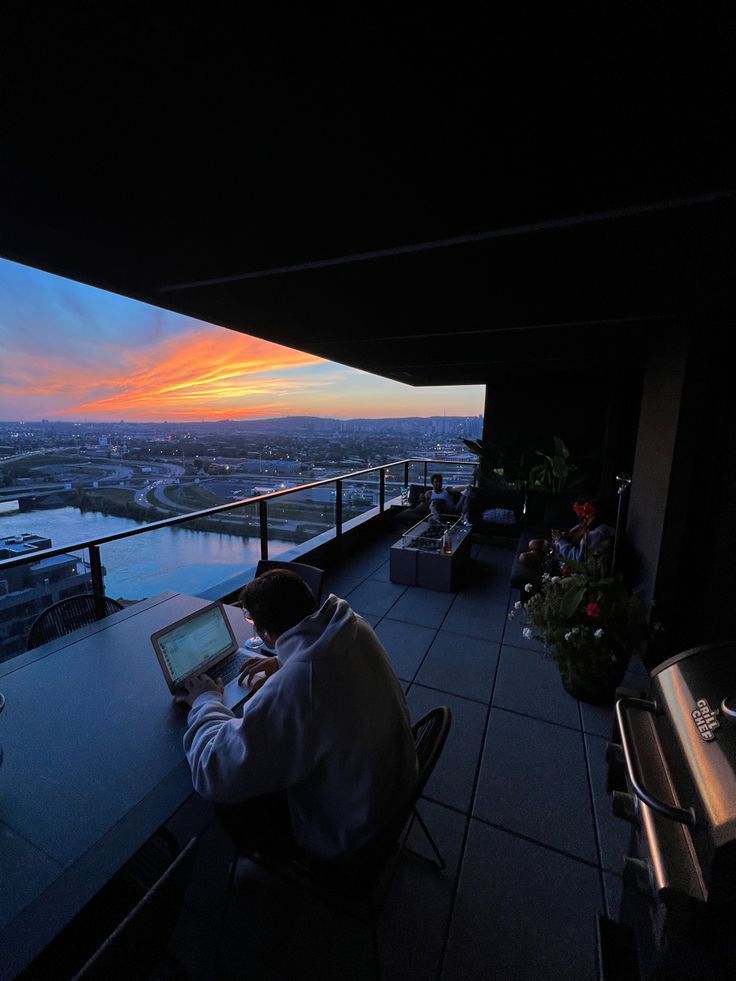 man on laptop wearing light gray oversized hoodie. sitting on balcony.jfif__PID:19bf2f15-6635-4d5d-a548-ebd726eece62